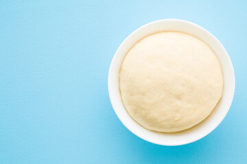 Fresh raw dough in bowl on light blue table background. Pastel color. Ready for baking. Closeup. Empty place for text. Top down view.