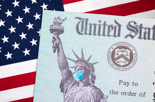 United States IRS Stimulus Check With Statue Of Liberty Wearing Medical Face Mask Resting On American Flag