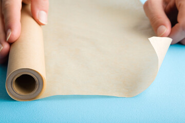 Young adult woman hands using roll of baking paper on light blue table background. Pastel color. Closeup.