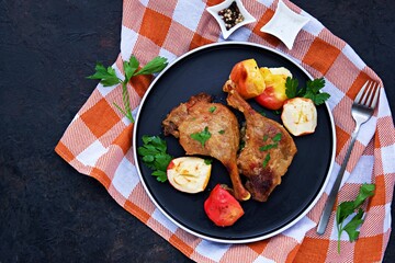 Baked duck leg with apples on a black plate on a dark concrete background. Christmas and New Years concept. Duck recipes. Thanksgiving Day.