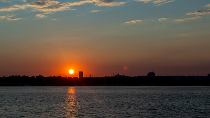 Fototapeta premium sunset, in the foreground the river, in the background the sun sets over the city