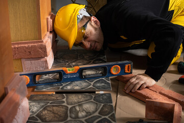A construction worker checks with a spirit level that the terracotta tiles are evenly placed in all areas. Dressed in personal protective equipment.