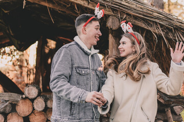 A couple about their appearance are dressed in New Year's hoops on their heads, holding a sparkler in their hands and smiling at each other against the background of a gazebo made of firewood