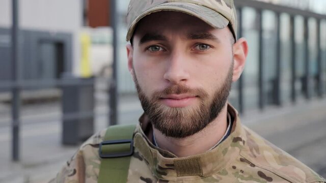 Portrait shot of serious caucasian soldier young male soldier in cap with backpack posing to camera at the railway station. Going to army.