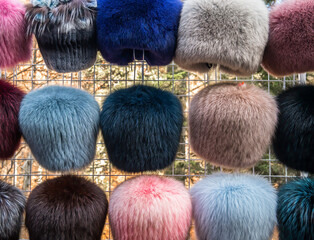 Colored (synthetic) woman's fur hats on display outdoor on a fence.