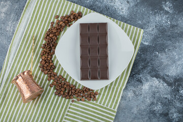Bar of chocolate with coffee beans on a tablecloth