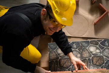 The builder applies brick-shaped decorative tiles to the furniture board and checks if they fit exactly. Construction worker wearing personal protective equipment.