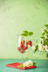Fresh ripe raw strawberry with green leaves in the wine glass on green surface.