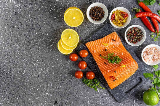 Raw salmon fillet and ingredients for cooking, seasonings and herbs on a dark background
