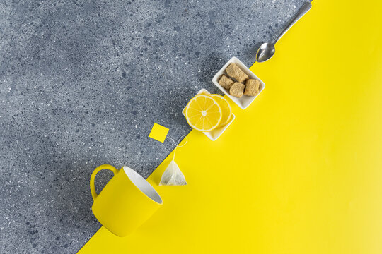 Creative tea food background of Ultimate Gray and Illuminating trending color. Tea, lemon, cup and spoon on gray and yellow table surface, top view.
