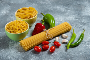 Raw pasta with fresh vegetables on a gray background