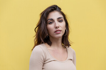 Obraz premium Smiling young brunette woman on the background of a yellow wall of a building. Lifestyle.