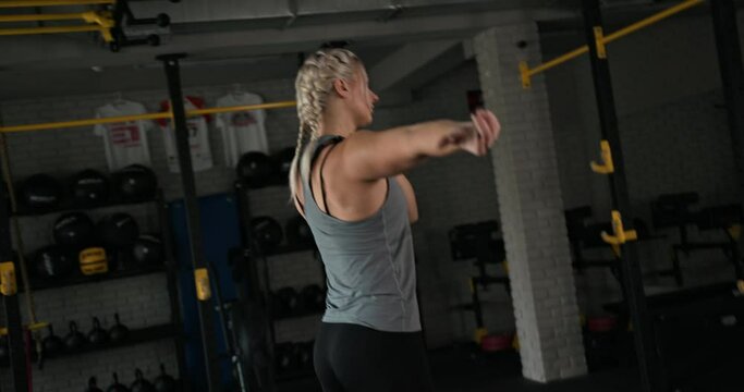 Sportswoman stretching arms in gym. Female athlete with blond braids doing warm up exercise during fitness workout in gym