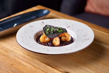 Black rice risotto. Shrimp risotto on a white plate on the table, serving in a restaurant, menu food concept