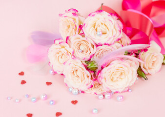 delicate bouquet of bushy peony roses with bright ribbons, pearls, feathers and hearts  on a pink background, the concept of congratulations on Valentine's day