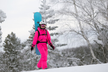 Fototapeta na wymiar Woman in bright pink sportive overall with snowboard on the backpack having fun outisde in snowy day. Winter restorative escape concept.