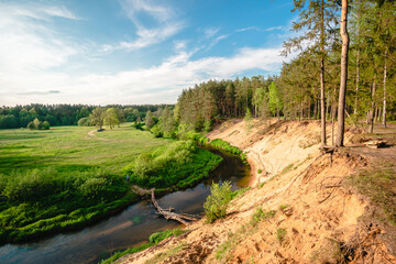 Obraz premium River landscape. Beautiful view of river from the high steep Bank, overgrown with grass. beautiful Sunny landscape of the river with high banks, blue sky and green grass of summer
