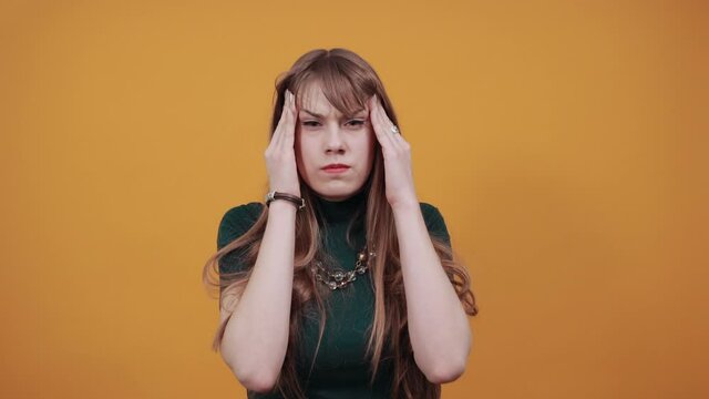 Headache grimacing pain holds the back of neck indicating location. Fatigue during workaholism labor. Young attractive woman, dressed green shirt blonde hair, yellow background