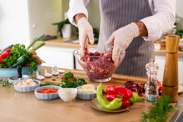 The cook mixing the spices and the meat for burger with onion and bacon in a bowl