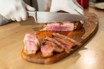 A close-up of a chef cutting a grilled steak on a wooden board