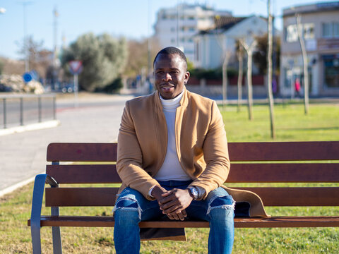 Hombre negro elegante sentado en un banco en la calle