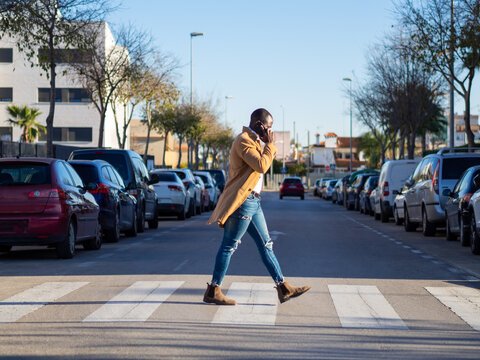 Hombre negro cruzando la calle mientras habla con el teléfono móvil