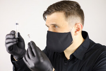 a man wearing black medical gloves and a protective mask holds a syringe for injectio on a white...