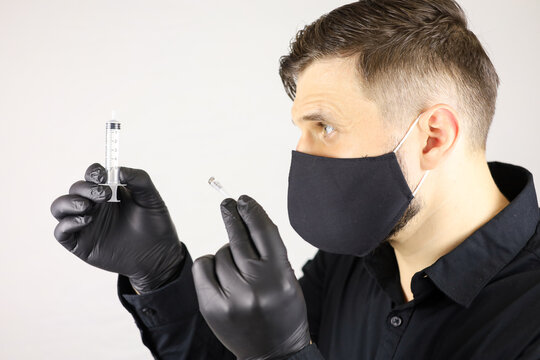 a man wearing black medical gloves and a protective mask holds a syringe for injectio on a white background