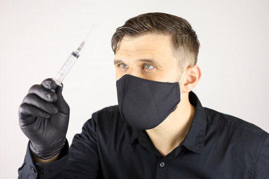 a man wearing black medical gloves and a protective mask holds a syringe for injectio on a white background