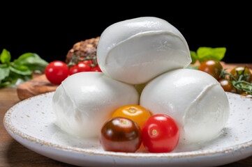 Cheese collection, white balls of soft Italian cheese mozzarella, served with red cherry tomatoes, fresh basil leaves