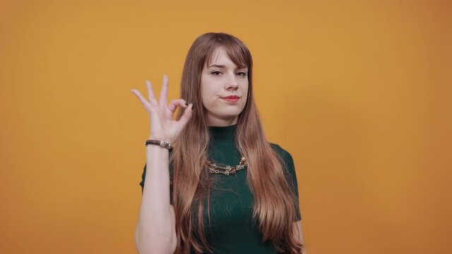 View of hand fingers showing ok sign, gesturing making okay, human emotions, facial expressions, feelings. Young attractive woman, dressed green shirt blonde hair, yellow background