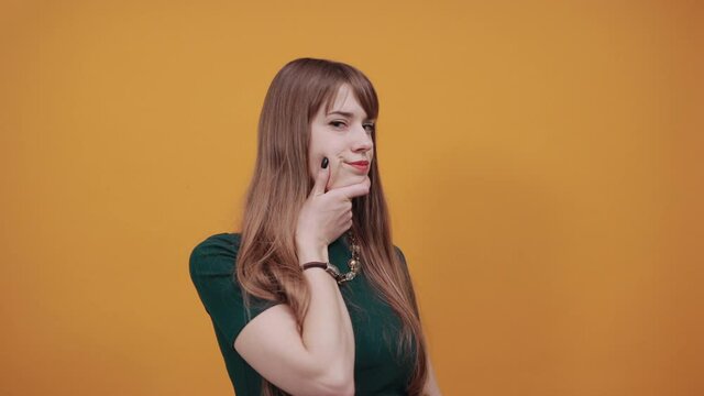 Hand on chin thinking about question, pensive expression. Doubt. Thoughtful face. Using that incredibly sharp business mind. Young attractive woman, dressed green shirt blonde hair, yellow background