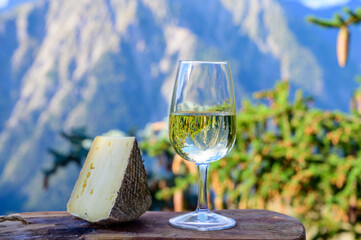 Glass of swiss or savoy dry white wine and tomme cheese with Alpine mountains peaks on background
