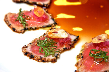 Tuna sashimi, Fried tuna steak with black sesame, olive oil and teriyaki sauce, served on white plate and wooden background, close up view