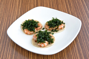 Mexican shrimp tacos with fried parsley, served on a white square plate on wooden background