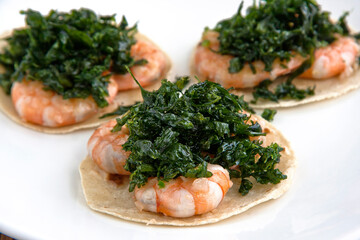 Mexican shrimp tacos with fried parsley, served on a white square plate on wooden background,close up
