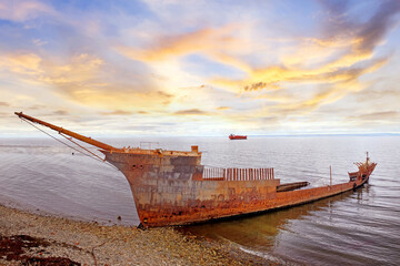 The wreck of the Frigate Lord Lonsdale beached on the shores of Punta Arenas, during a warm sunset, against a colorful sky covered by dramatic clouds.