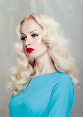 Fototapeta premium Profile portrait of a beautiful young blonde woman with curly hair and makeup, red lips, dressed in a blue dress.