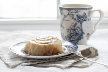 Original lifestyle still life photograph of a warm homemade cinnamon rolls on a plate with a fork and a cup of tea in front of a sunny window