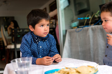 Handsome little gentlemen wearing the bow tie on a party with his brother, children at a party table