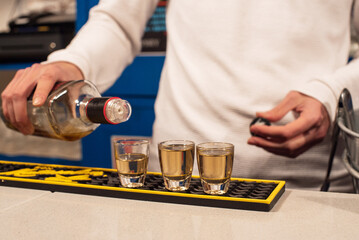 Un camarero joven llena unos vasos de chupito de una bebida alcohólica de color marrón en la barra de un bar