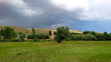 Distant and pastoral view of a village in Anatolia, Turkey with clouds in the sky, tress and mosque.
