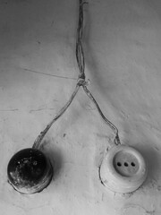 Black and white electric wires, old vintage plug socket and electric switch on a white wall.