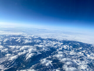 An aerial view from an airplane window of mountains, snow, clouds and blue skies.