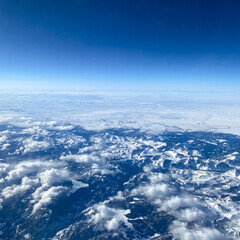 Naklejka na ściany i meble An aerial view from an airplane window of mountains, snow, clouds and blue skies.