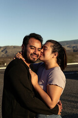 Side view portrait of a amazing couple kissing against sunset outside while traveling in their vacation time. Mexican couple kissing mountains view behind them