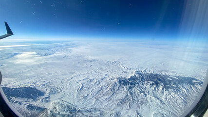 Fototapeta na wymiar An aerial view from an airplane window of mountains, snow, clouds and blue skies.