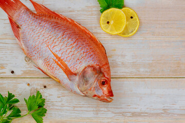 Raw red tilapia fish with herbs and lemon and lime on wooden background. Top view.