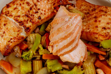 Close up of baked salmon fillet with steamed vegetables.