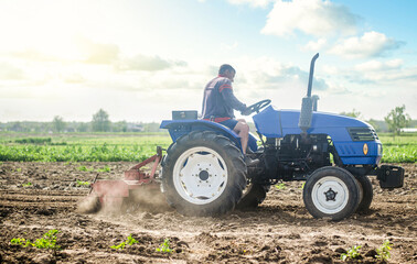 A farmer on a tractor works in the field and raises dust. Plowing field. Use of agricultural machinery and to simplify and speed up work. Loosening surface, land cultivation. Farming, agriculture. © Andrii Yalanskyi